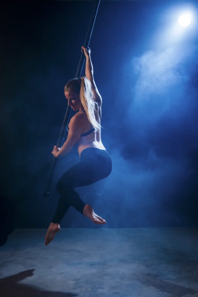 Madame Passions réalisant une figure de flying pole, accrochée par une barre tenue par le haut