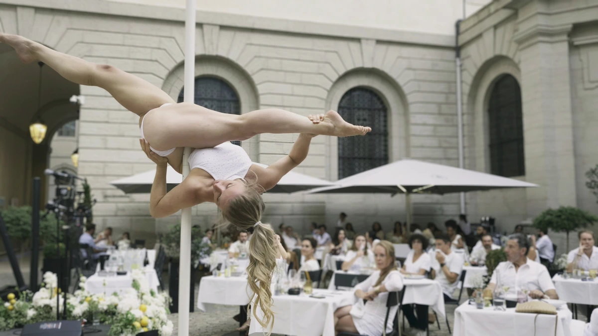 Performance de Pole Dance en plein air lors d’une soirée chic au restaurant Le Grand Réfectoire à Lyon. La danseuse, en tenue blanche, exécute une figure aérienne devant un public élégant en terrasse, dans la cour intérieure de l’Hôtel Dieu.