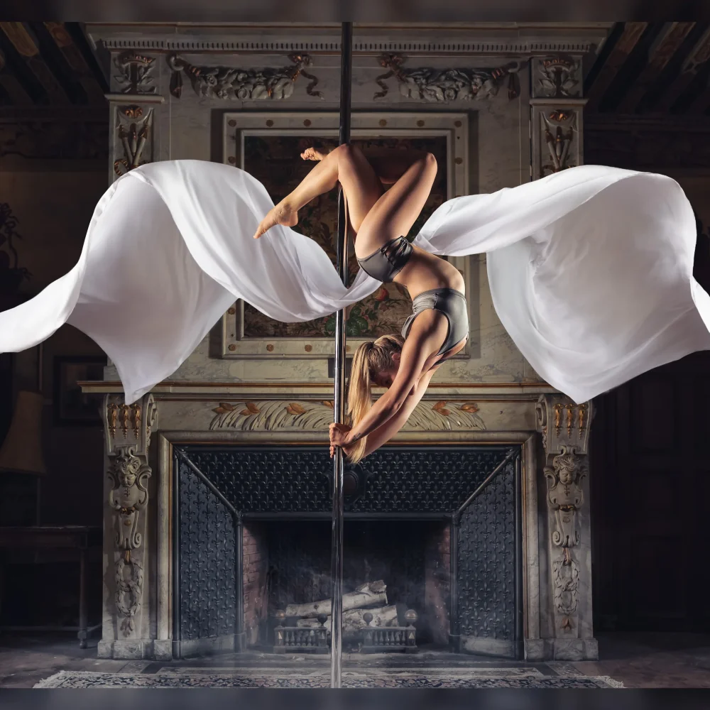 Madame Passions réalisant une figure de pole dance dans une tenue artistique avec des voiles